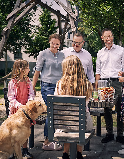Zwei Männer, eine Frau, zwei Mädchen und ein Hund beim Picknick im Freien an einem Holztisch