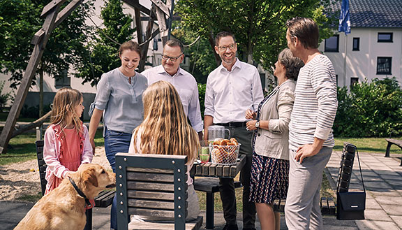 Zwei Männer, eine Frau, zwei Mädchen und ein Hund beim Picknick im Freien an einem Holztisch