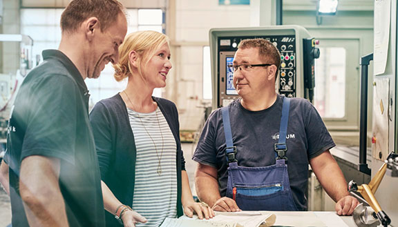 Unternehmerin Melanie Baum bespricht sich mit zwei Mitarbeitern in einer Werkstatt vor einer Maschine.