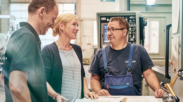 Unternehmerin Melanie Baum bespricht sich mit zwei Mitarbeitern in einer Werkstatt vor einer Maschine.