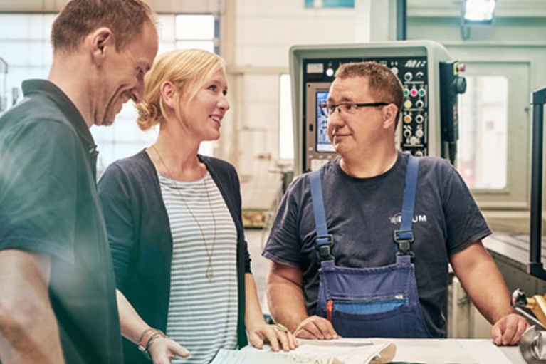 Unternehmerin Melanie Baum bespricht sich mit zwei Mitarbeitern in einer Werkstatt vor einer Maschine.