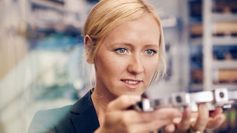 Unternehmerin Melanie Baum hält ein Metallteil auf ihrer Produktion in den Händen und betrachtet es.