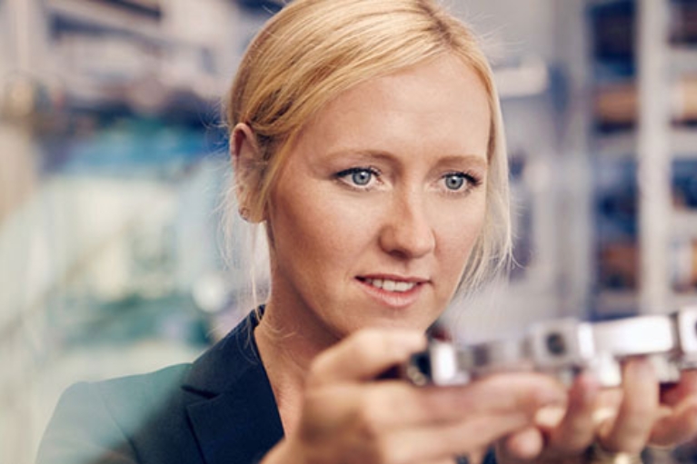 Unternehmerin Melanie Baum hält ein Metallteil auf ihrer Produktion in den Händen und betrachtet es.