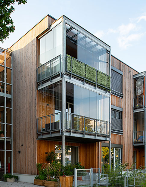 Holzfassade mit großen Glasflächen und Balkonen, moderner Wohnbau mit Begrünung.