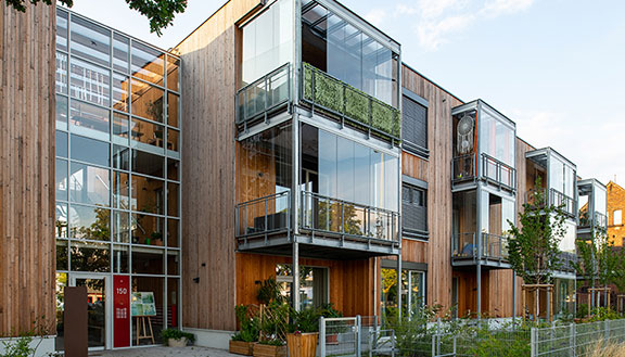 Holzfassade mit großen Glasflächen und Balkonen, moderner Wohnbau mit Begrünung.