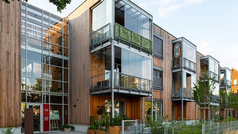Holzfassade mit großen Glasflächen und Balkonen, moderner Wohnbau mit Begrünung.