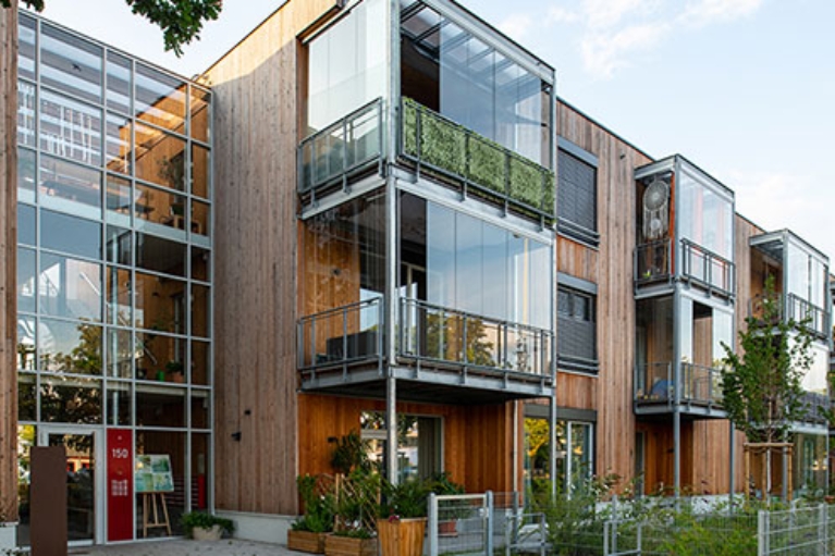 Holzfassade mit großen Glasflächen und Balkonen, moderner Wohnbau mit Begrünung.