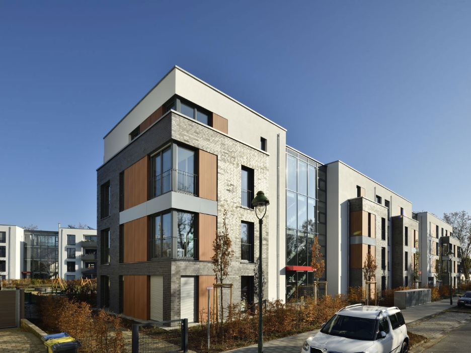 Modernes, neu gebautes Wohnquartier, davor Vorgärten mit kleinen Bäumen, im Hintergrund ein Spielplatz