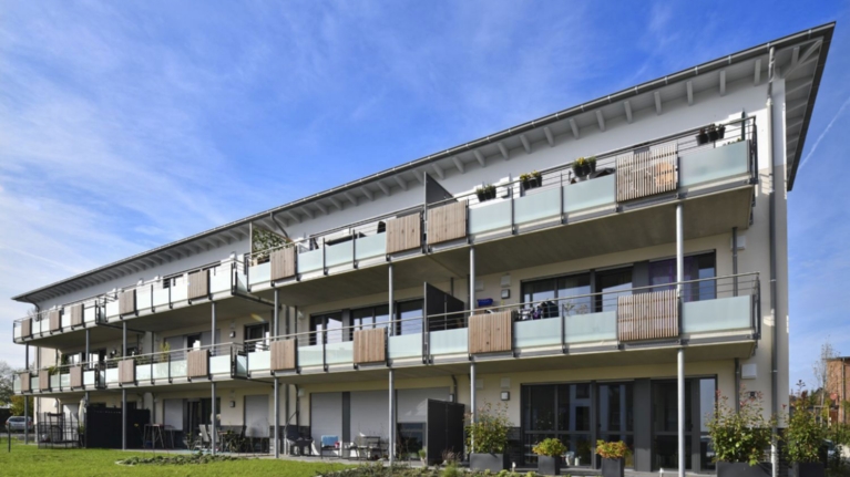 Rückseite eines Mehrfamilienhauses mit Balkonen, Terrassen, Garten und einem Beet