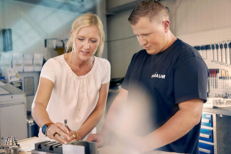 Unternehmerin Melanie Baum und ein Mitarbeiter in einer Werkstatt, sie zeigt ihm die Bearbeitung eines Metallteils.