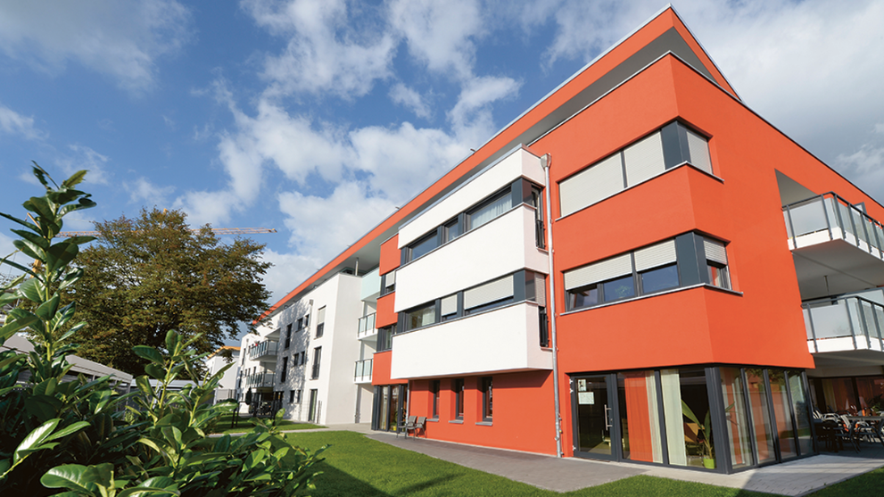 Moderner Neubau eines Wohnblocks mit rot-weißer Fassade und Garten