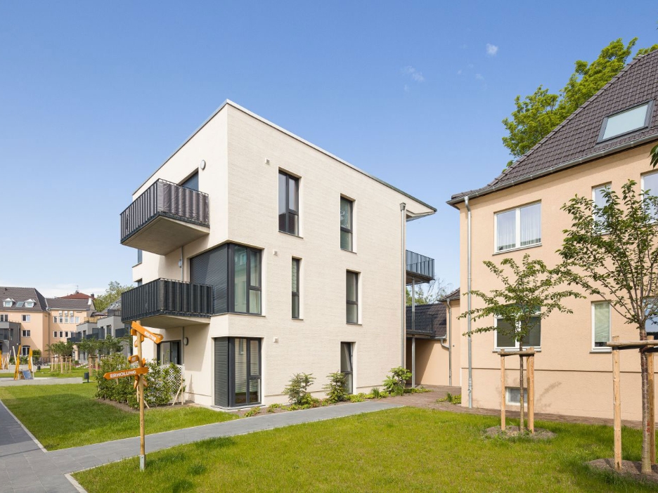 Weißes Mehrfamilienhaus mit Rasen im Vorgarten und davor verlaufendem Fußweg