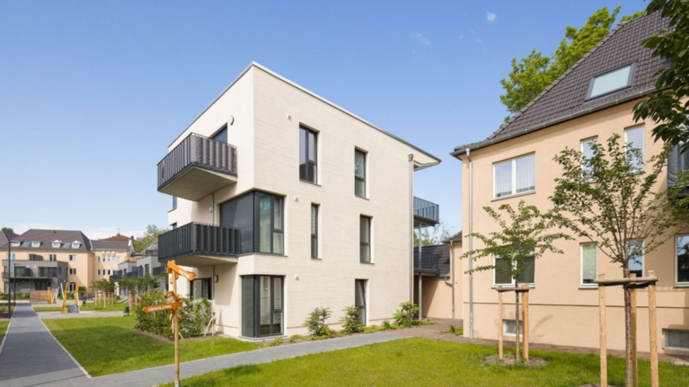 Weißes Mehrfamilienhaus mit Rasen im Vorgarten und davor verlaufendem Fußweg