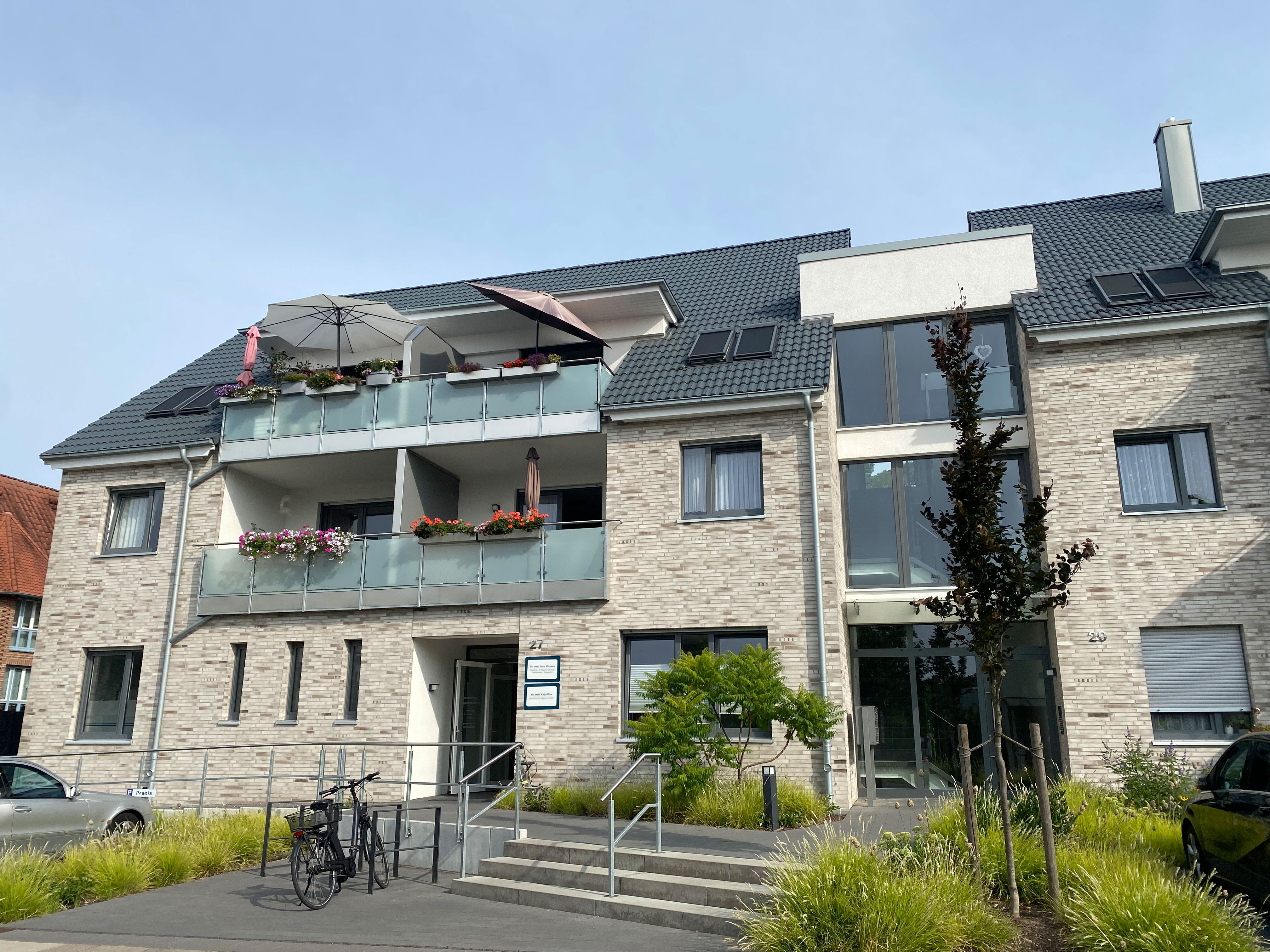 Modernes Mehrfamilienhaus mit grauer Klinkerfassade, davor parkende Autos und ein Fahrrad