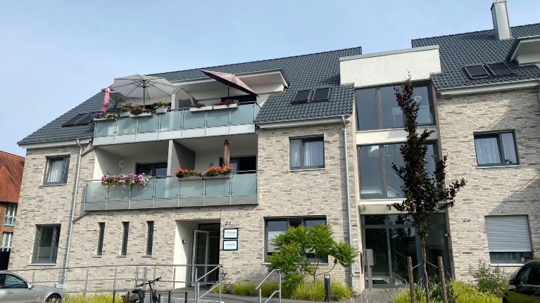 Modernes Mehrfamilienhaus mit grauer Klinkerfassade, davor parkende Autos und ein Fahrrad