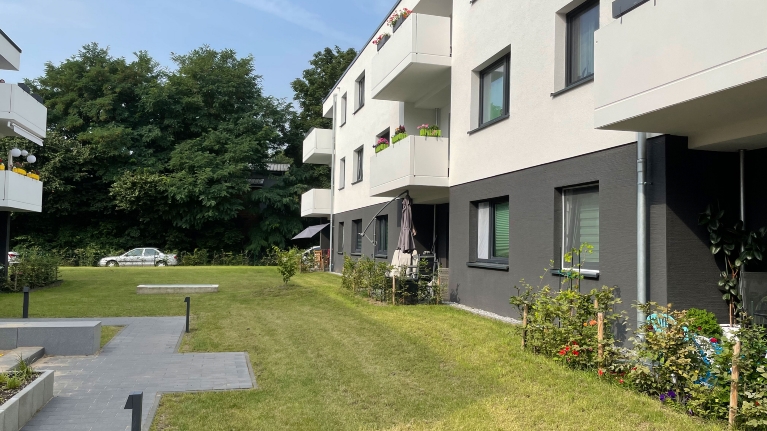 Schwarz-weiße Fassade eines Wohnquartiers, davor eine Rasenfläche und kleine Vorgärten