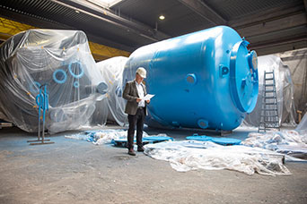 InProCoat-Geschäftsführer Dr. Jörg Doege in einer Werkshalle vor einem großen blauen Metalltank