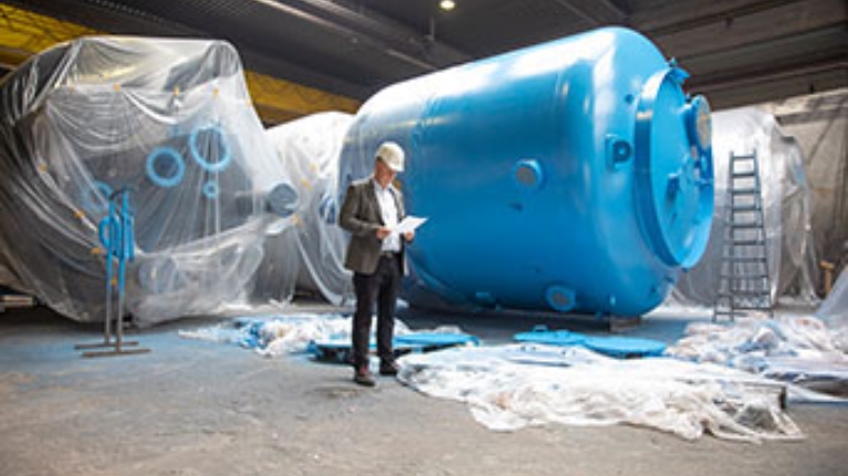 InProCoat-Geschäftsführer Dr. Jörg Doege in einer Werkshalle vor einem großen blauen Metalltank