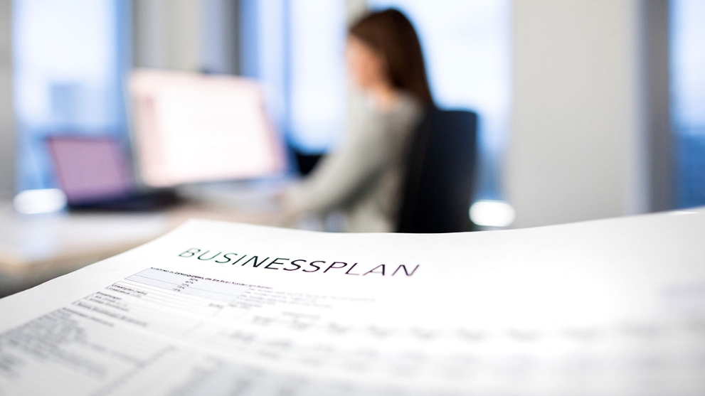 Ausdruck eines Businessplans, im Hintergrund eine Frau an einem Schreibtisch