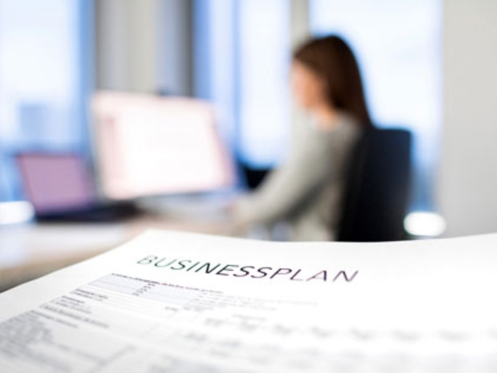 Ausdruck eines Businessplans, im Hintergrund eine Frau an einem Schreibtisch