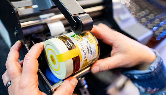 Ein Glas mit veganem Honig in einer Etikettiermaschine