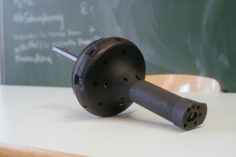 Thermoscan-Messgerät liegt auf einem Tisch. Optisch erinnert es an eine Fackel.