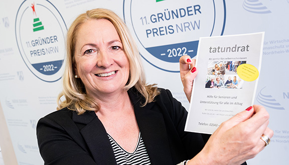 Die Nominierte des Gründerpreises 2022 Sabine Paschen-Schnarkowski der Initiative tatundrat steht vor der Medienwand und hält eine Papier mit Informationen zu der Initiative hoch.
