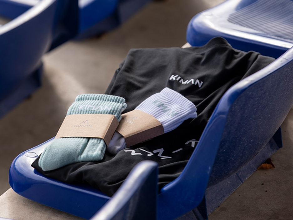 Gefaltetes schwarzes T-Shirt und zwei Paar Socken mit Papierband liegen auf blauen Stadionsitzen.