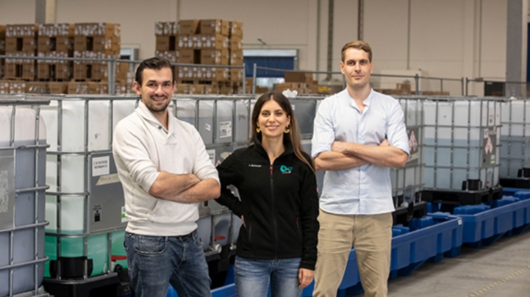 Das Gründungsteam von cylib steht in einer Lagerhalle vor Containern und lächelt in die Kamera.