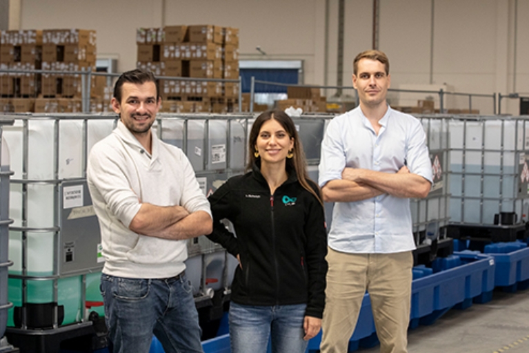 Das Gründungsteam von cylib steht in einer Lagerhalle vor Containern und lächelt in die Kamera.