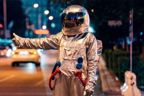 Mann in einem Astronautenanzug in Anhalterpose an einer Straße