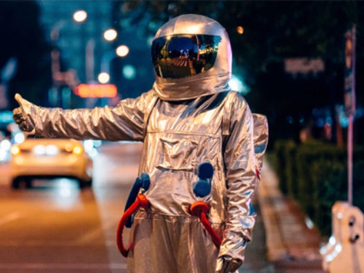 Mann in einem Astronautenanzug in Anhalterpose an einer Straße