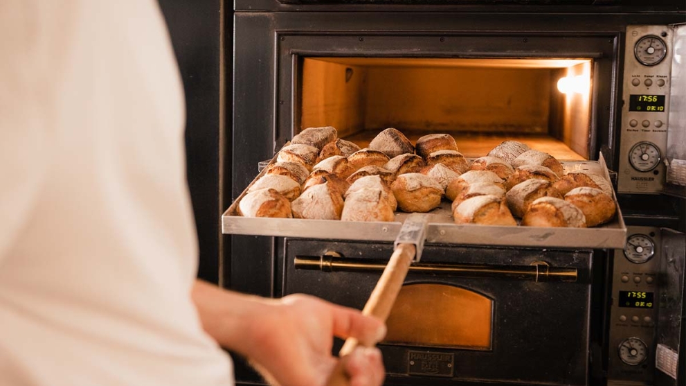 Jemand holt frisch gebackene Brötchen aus dem Backofen einer Bäckerei.