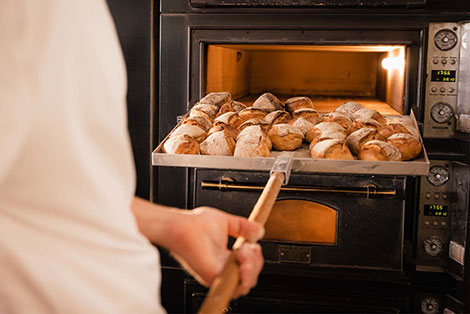 Jemand holt frisch gebackene Brötchen aus dem Backofen einer Bäckerei.