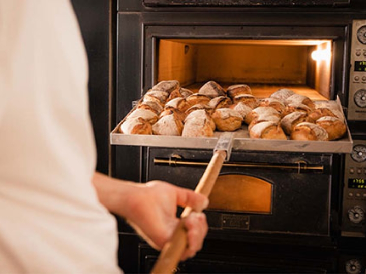 Jemand holt frisch gebackene Brötchen aus dem Backofen einer Bäckerei.