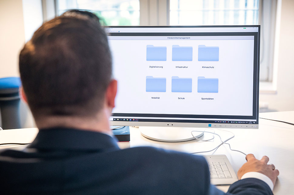 Ein Mann sitzt vor einem Monitor, der ein Programm zum Fördermittelmanagement zeigt.