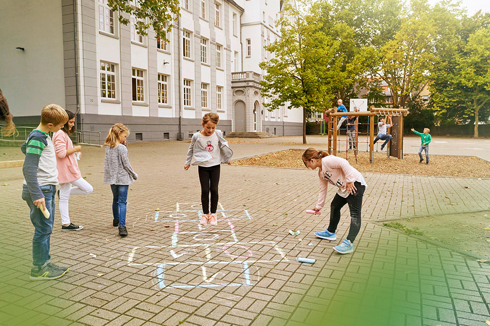 Auf dem Bild sieht man mehrere Kinder auf dem Schulhof. Die NRW.BANK hat den Ausbau der kommunalen Infrastruktur gefördert.
