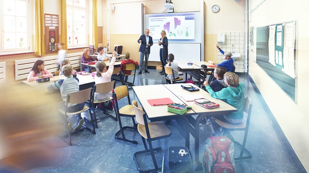 Unterrichtsraum einer Schule mit lernenden Schülern an drei Tischen.