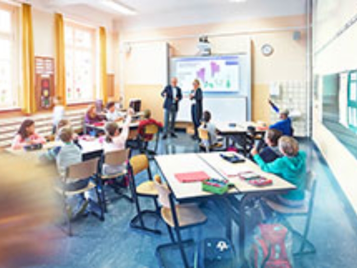 Unterrichtsraum einer Schule mit lernenden Schülern an drei Tischen.