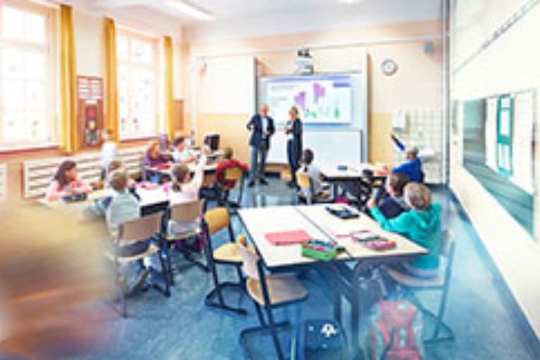 Unterrichtsraum einer Schule mit lernenden Schülern an drei Tischen.