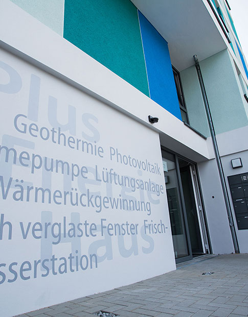 Plus-Energie-Haus in Bottrop mit der Aufschrift: „Plus Energie Haus“ und den Schlagworten Geothermie, Photovoltaik, Wärmepumpe, Lüftungsanlage mit Wärmerückgewinnung, 3-fach verglaste Fenster, Frischwasserstation.