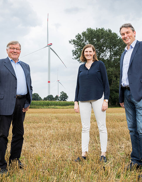 Bernhard Wieker, Theresa Ungru und Hermann Willers von der Hörstel GmbH & Co. KG stehen vor Windkraftanlagen, die durch NRW.BANK.Energieinfrastruktur gefördert wurden.
