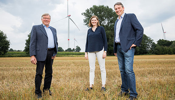Bernhard Wieker, Theresa Ungru und Hermann Willers von der Hörstel GmbH & Co. KG stehen vor einer Windkraftanlage.