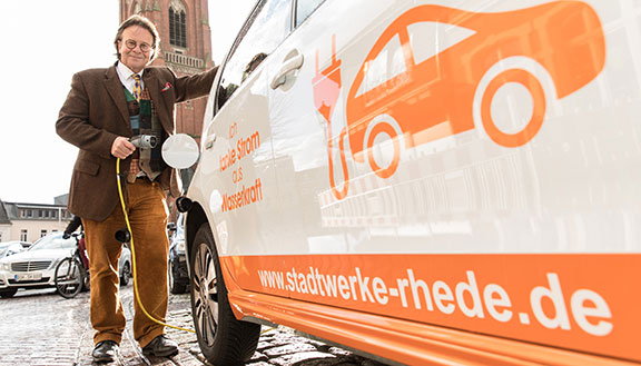 Dr. Ronald Heinze, Geschäftsführer der Stadtwerke Rhede, lädt ein Elektrofahrzeug.