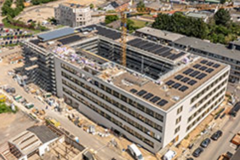 Luftaufnahme einer großen Rathaus-Baustelle mit Kran und umliegender Stadtinfrastruktur.