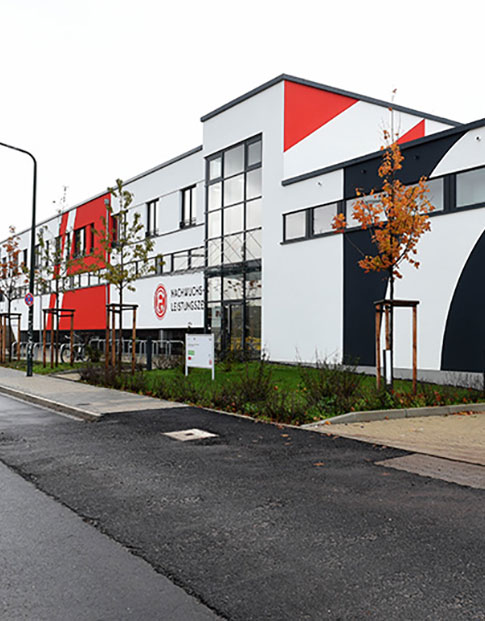 Neubau eines Trainingszentrums mit rot-weißer Fassade und Fortuna Düsseldorf Logo.