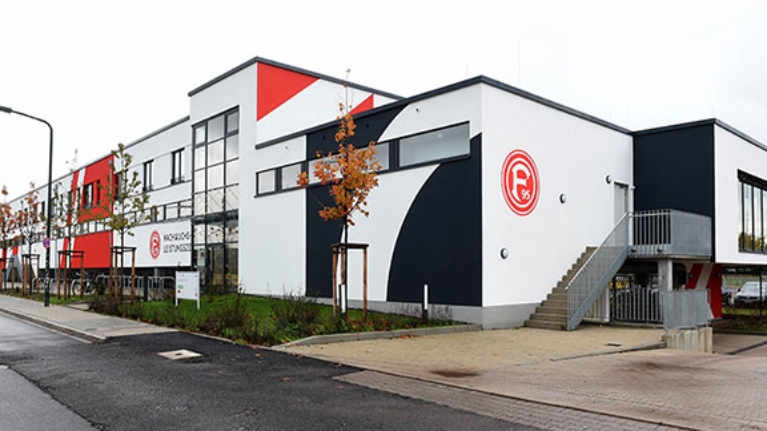 Neubau eines Trainingszentrums mit rot-weißer Fassade und Fortuna Düsseldorf Logo.
