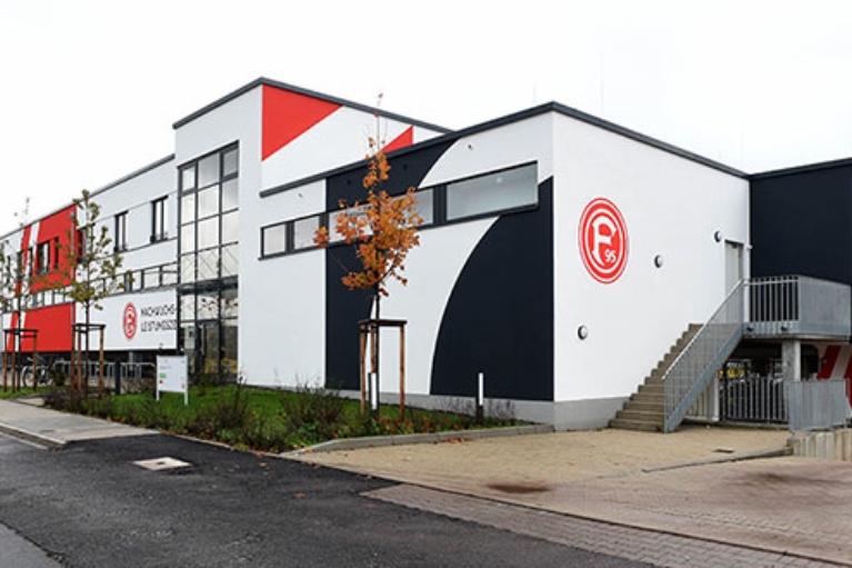 Neubau eines Trainingszentrums mit rot-weißer Fassade und Fortuna Düsseldorf Logo.