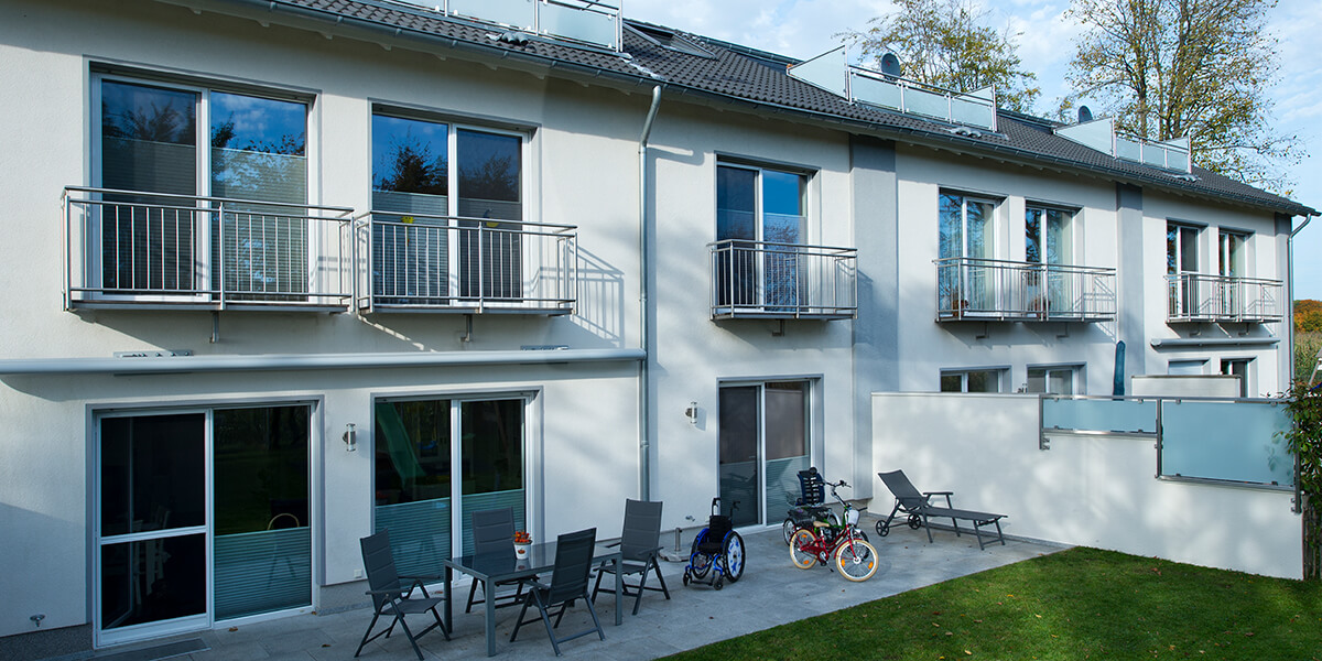 Rückansicht einer Eigenheimsiedlung mit Terrassenmöbeln, einem Kinderfahrrad und eines Rollstuhls