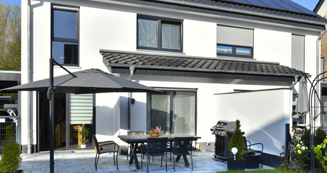 Ein weißes Einfamilienhaus mit schwarzem Dach, auf dem Solarpanel installiert sind.